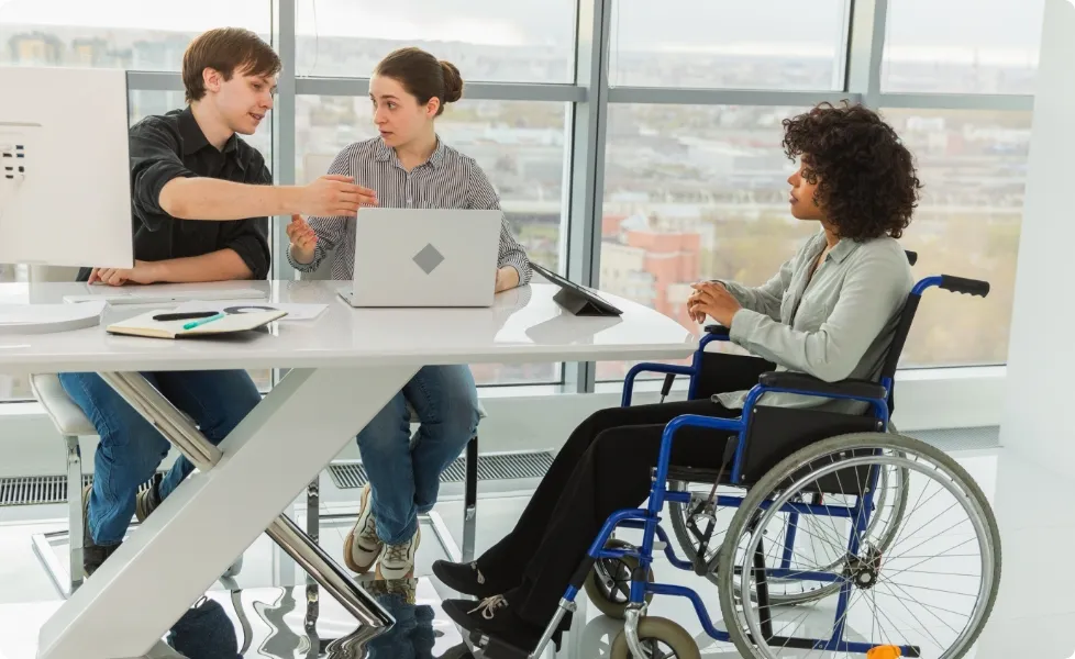 An employee using a wheelchair collaborating with colleagues in a bright office meeting.